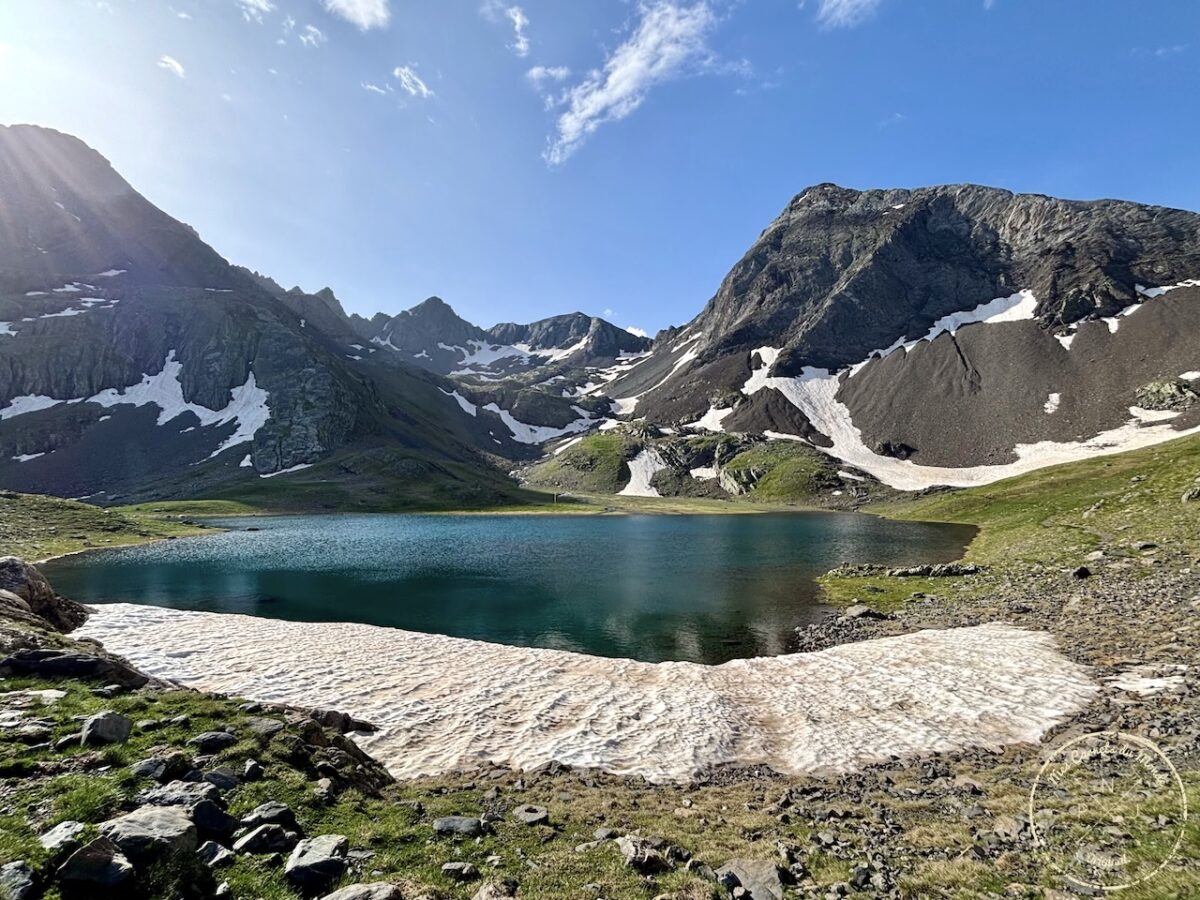 Lac de montagne aux eaux bleues, avec un névé en bordure, au pied de la montagne, sous le ciel bleu dans les pyrénées