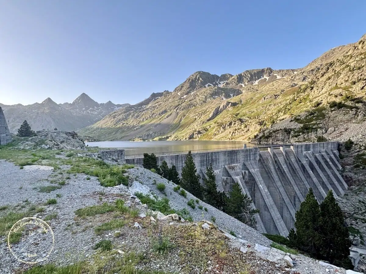 Barrage de Respomuso : avec des sapins au pied de la structure en béton, le lac et des montagnes enneigées autour du lac