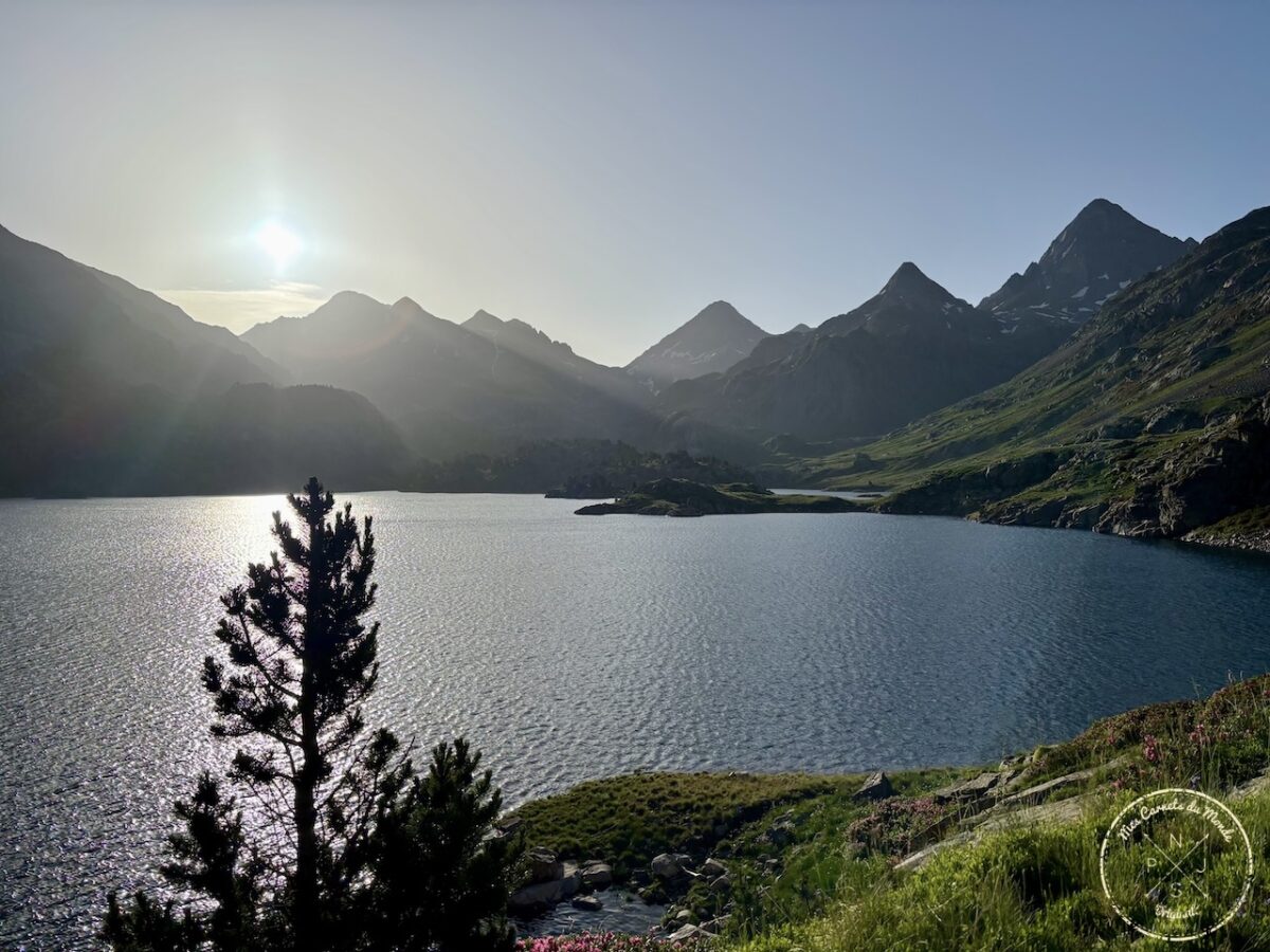 Lac de Respomuso, aux eaux bleu foncé, avec un sapin devant, le soleil levant sur les sommets enneigés